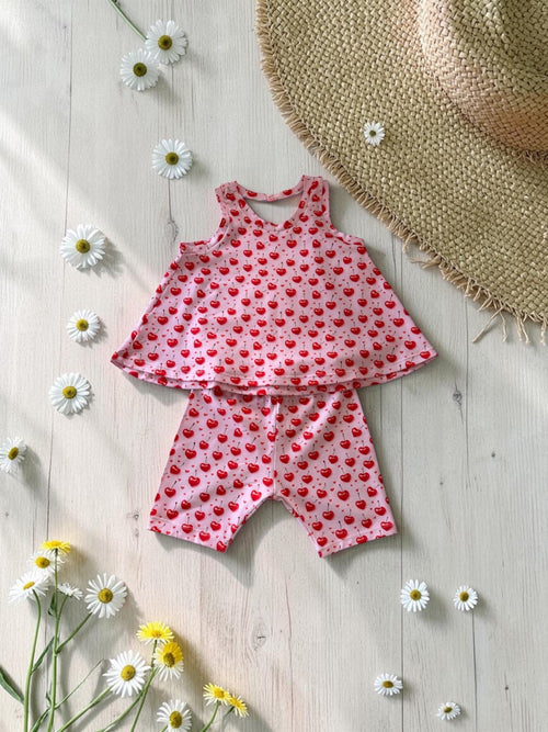 Children's swimsuit with cherry pattern on a wooden surface with flowers and a hat.