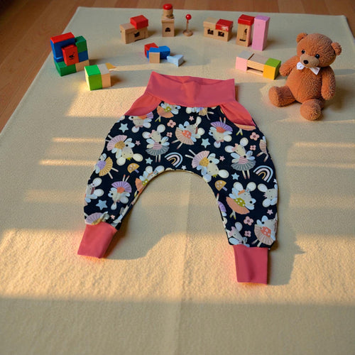 Floral-patterned baby pants with pink cuffs on a light surface with toys around